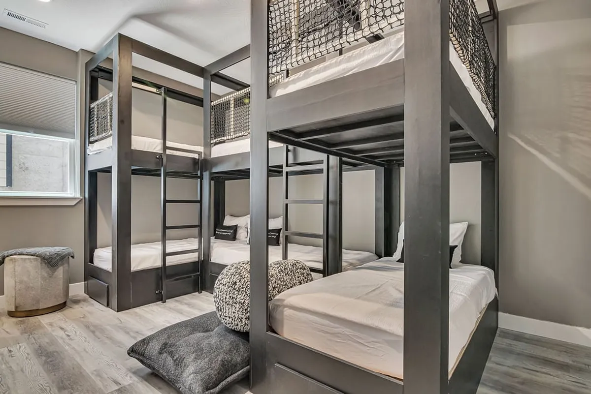 A cozy bunk room featuring stylish bunk beds, textured pillows, and a seating area that invites relaxation, reading, or play. The space is thoughtfully designed for kids or teens, striking a balance between fun and comfort.