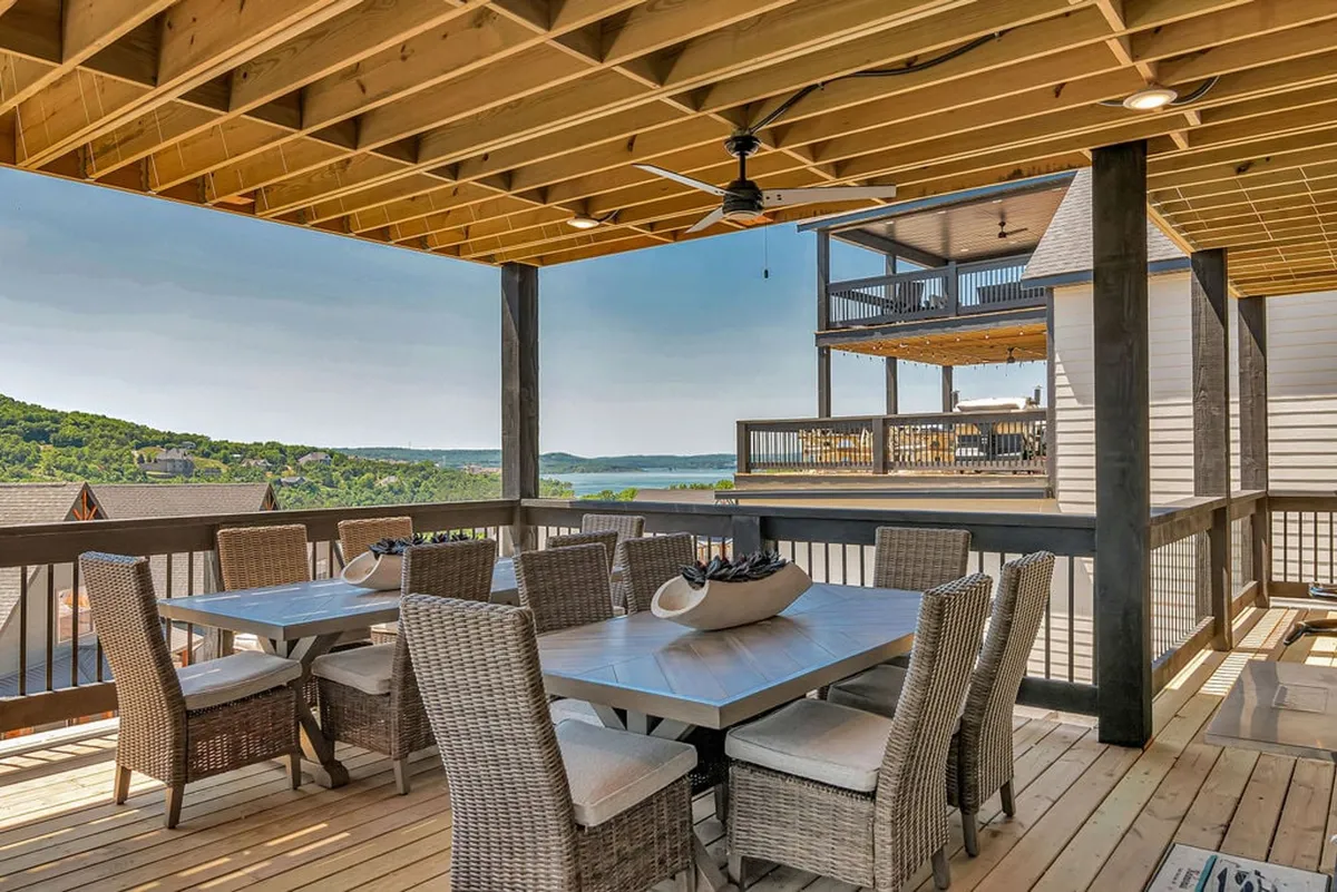 A lakeside outdoor dining area with a spacious table, surrounded by lush greenery and an open view toward Table Rock Lake. The setting is perfect for outdoor meals, barbecues, and soaking up the Ozark scenery. The relaxed mood invites gatherings after a day of adventure.