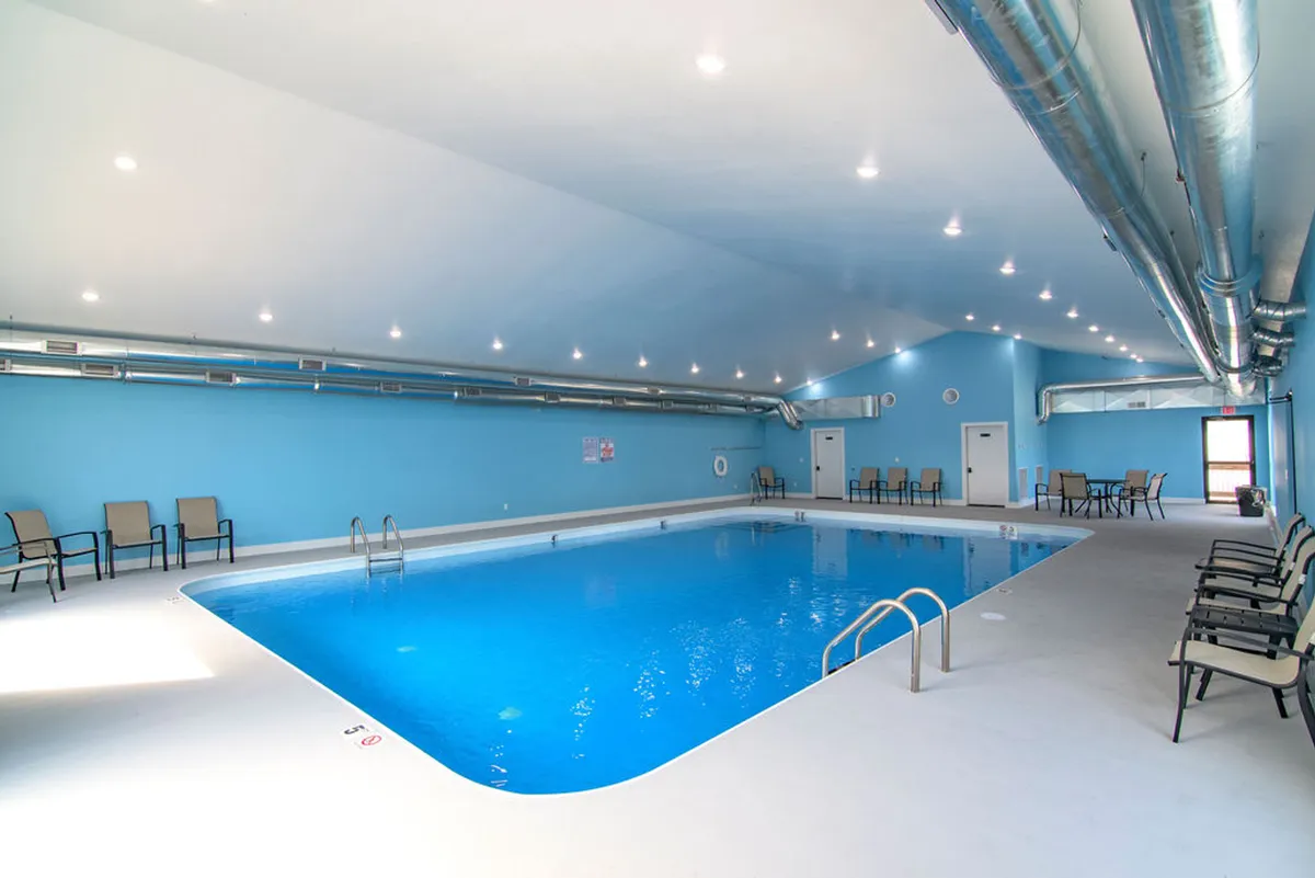 A bright, inviting indoor pool area with sparkling blue water, comfortable lounge chairs, and blue-toned walls, providing a tranquil and refreshing vibe ideal for family swimming year-round.