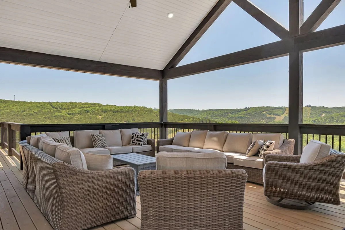 This exterior image showcases a large sectional sofa and coffee table set on a patio with a sweeping scenic view. The open-air setting invites relaxation and socializing, with hints of sunrise or sunset light, suggesting both early morning and evening enjoyment.