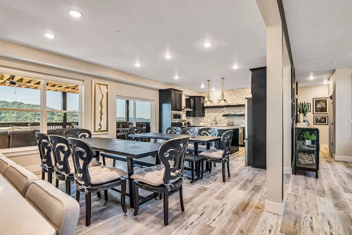 A stylish interior showing a large dining table, surrounded by chic black cabinetry and illuminated by floor-to-ceiling windows. Decor elements and wall art add sophistication, while the ample table size suggests the capacity for large family meals and celebrations.