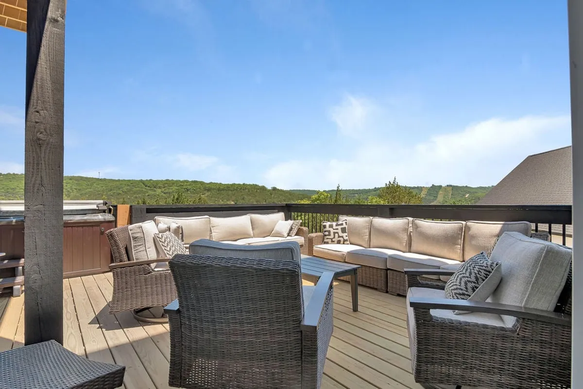 This image shows a welcoming outdoor seating area with comfortable lounge furniture and a hot tub, all set against a picturesque landscape view. The scene suggests relaxation and the ability to socialize or unwind while enjoying the outdoors.