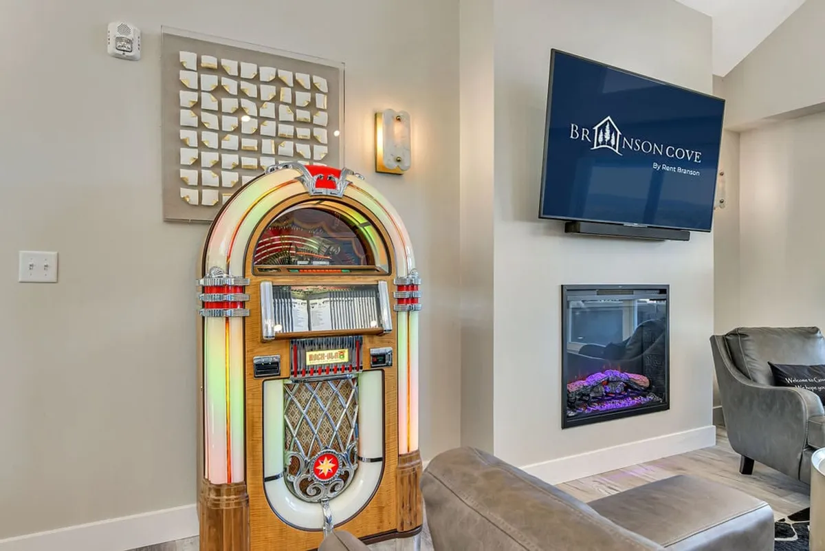 This image features a vintage jukebox, modern television, cozy seating area, and an electric fireplace, all set within a relaxed and cheerful atmosphere. The vibrant jukebox and the lounge space create a classic game room vibe.