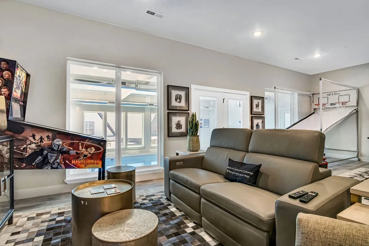 A playful lounge space with a comfortable sofa, prominent arcade game machine, basketball hoop, and decorative art, creating an atmosphere ideal for gaming, relaxing, and movie watching.