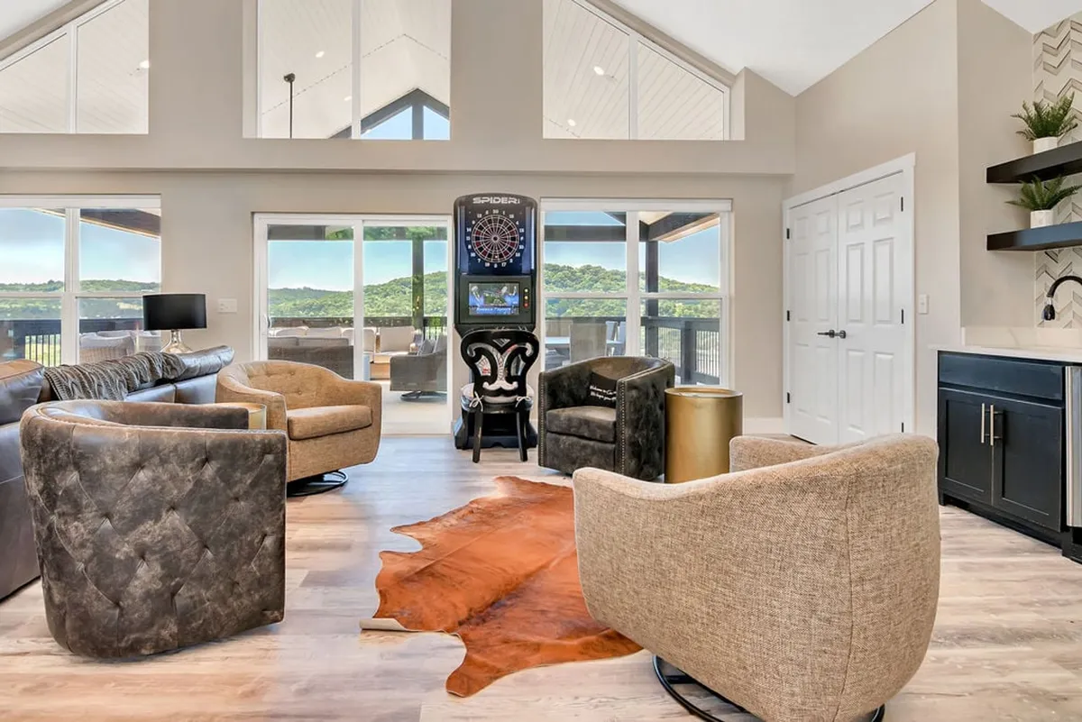 A dartboard machine is set against a wall, complemented by a cowhide rug and comfortable seating. The casual setup is ideal for friendly games and relaxing with friends, capturing the playful spirit of the Dad Cave.