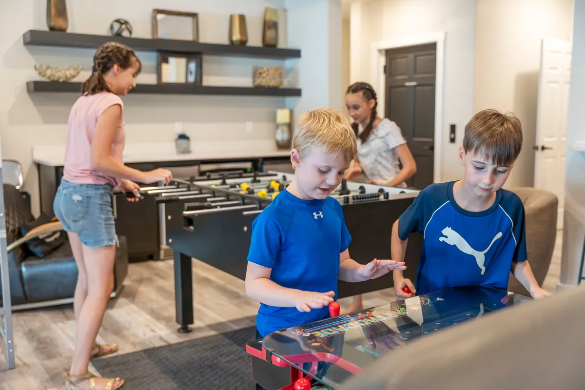 A lively game room scene featuring a foosball table, an arcade game, and children actively playing, with bright lighting and colorful decor that evoke a sense of fun and togetherness.