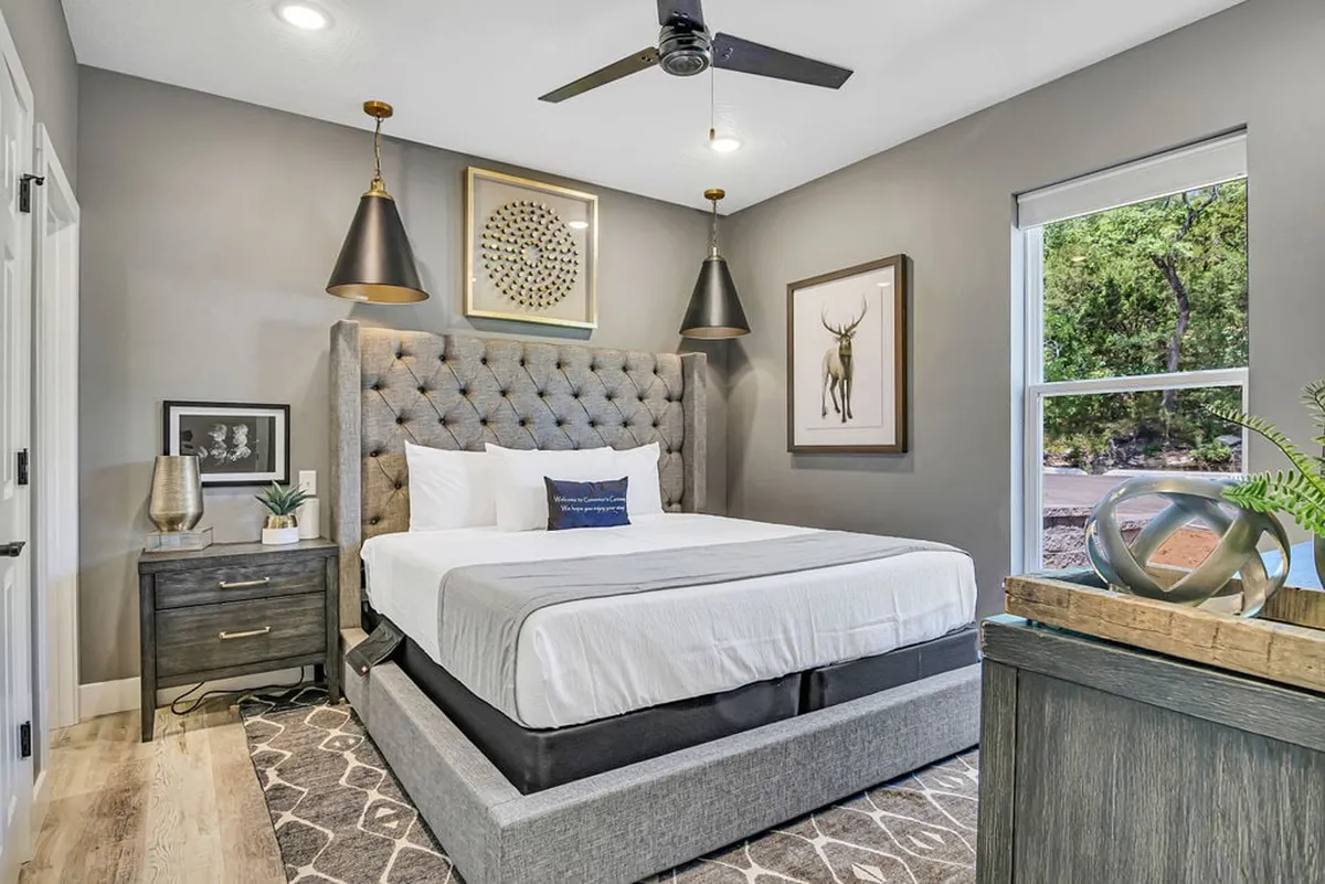 A serene king-sized bedroom with a tufted headboard, decorative wall art above the bed, stylish bedside lamps, and a large window that floods the space with natural light. The inviting atmosphere is enhanced by plush bedding and calming decor, reflecting the comfort of a premium suite.
