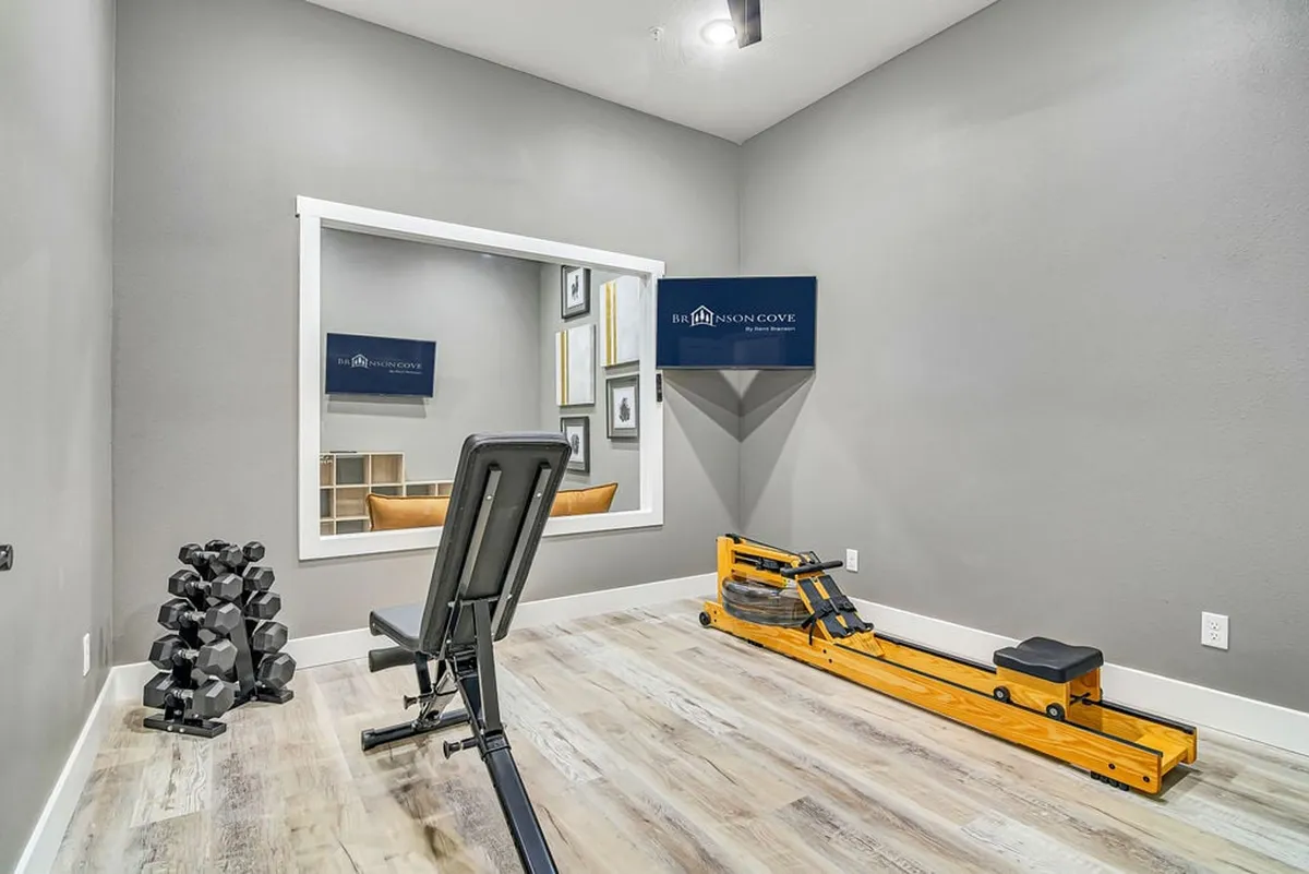 A well-equipped fitness room featuring a weight bench, dumbbells, a rowing machine, and a large wall mirror, offering an energetic space for workouts and wellness.